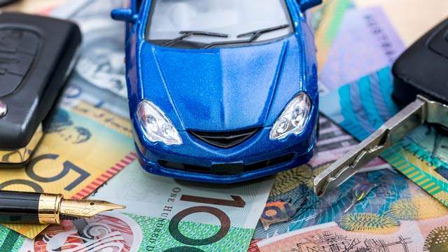 A blue toy car on some dollar bills next to car keys and a pen