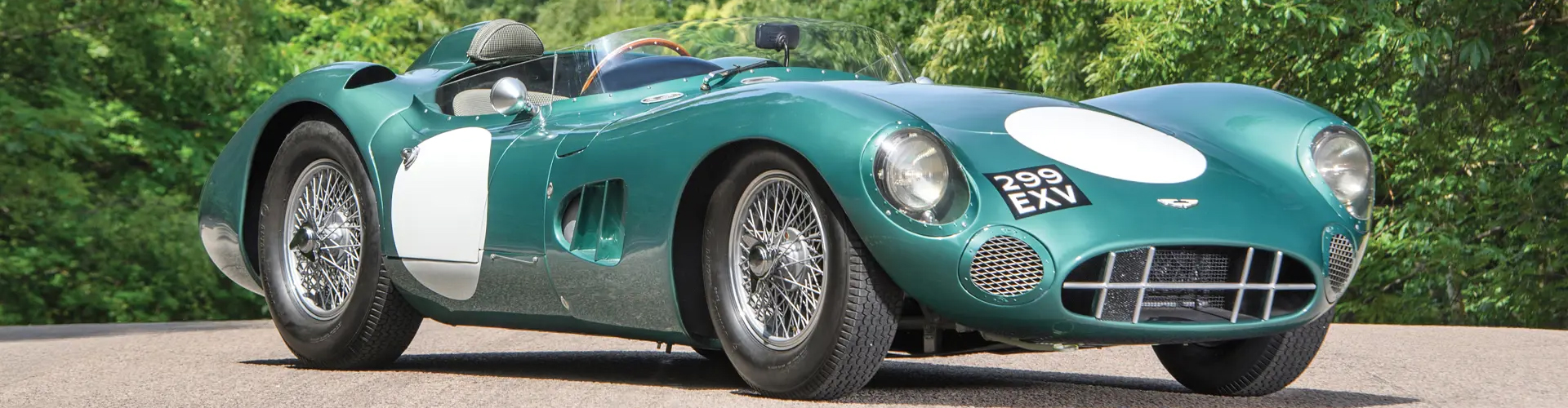 Turquoise and white Aston Martin DBR in front of trees