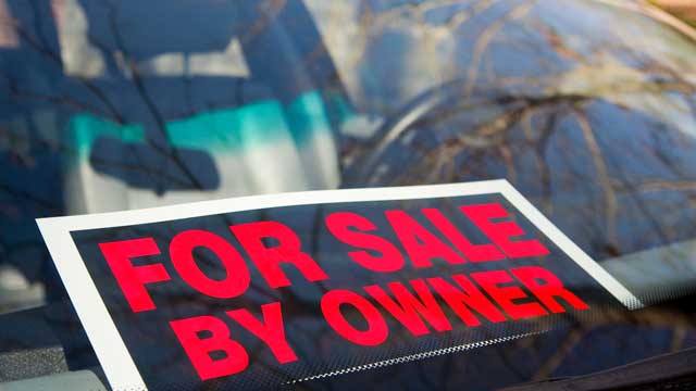 A sign in car window reads For Sale by Owner in large red letters