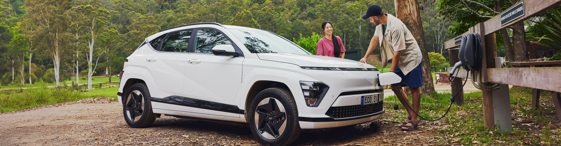 A couple charging a white EV in a bush location
