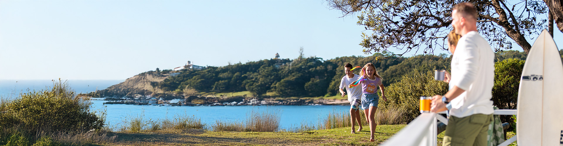A person stands at a deck as children run past by the beach