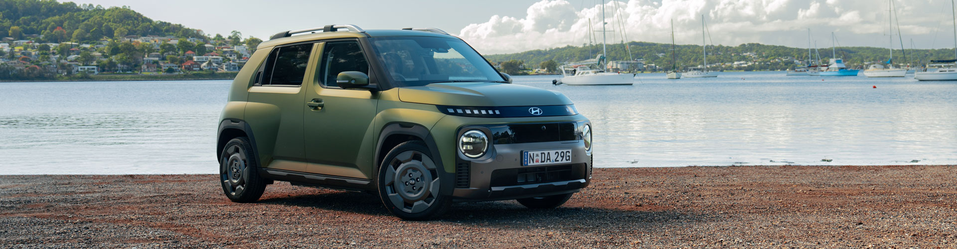 Metallic green 2025 Hyundai Inster Cross parked in front of marina