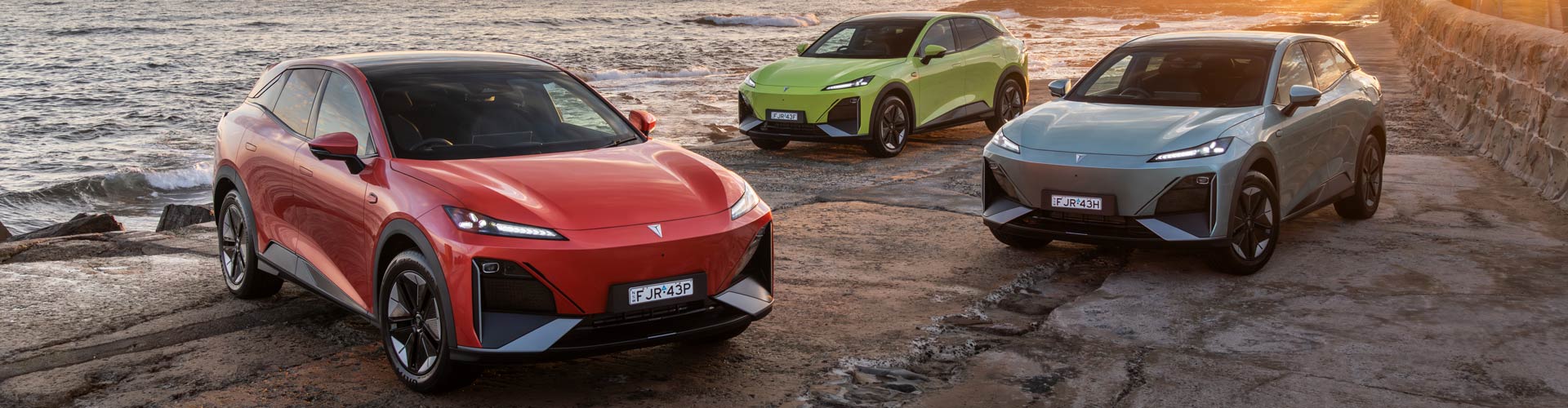 Three Deepal S07s in yellow, red and silver parked on a shorefront with sunset ocean scene behind