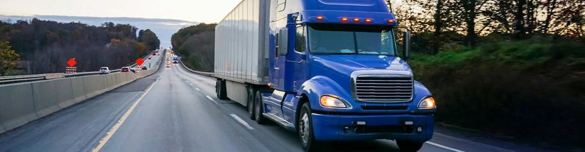 A large blue truck driving along the highway with a stretch of highway behind it.