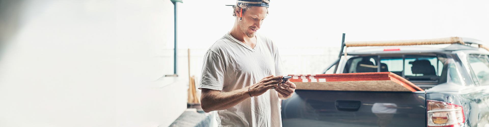 A man looking at his phone with a ute in the background - it's tray is full.