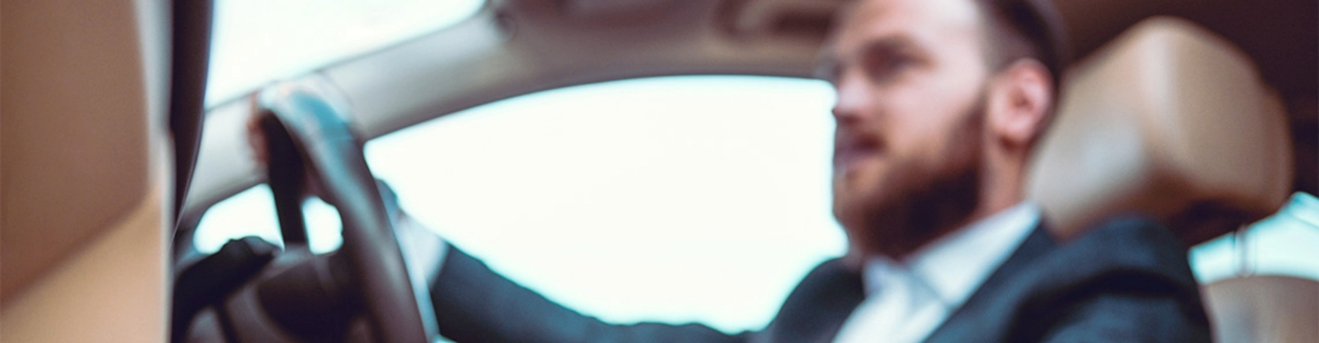 A man pictures in the driver's seat of a car, holding the steering wheel with one hand and the gear lever with his other hand.