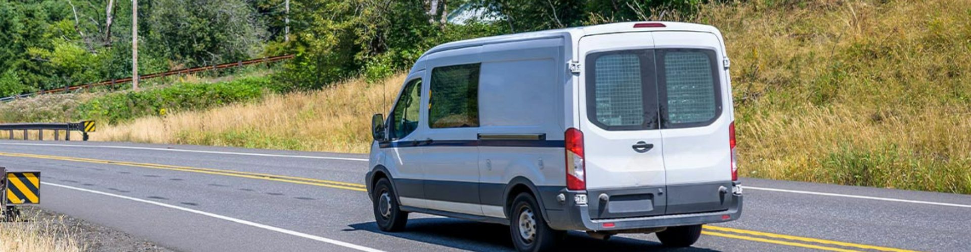 A white fleet vehicle driving along a highway on a sunny day.