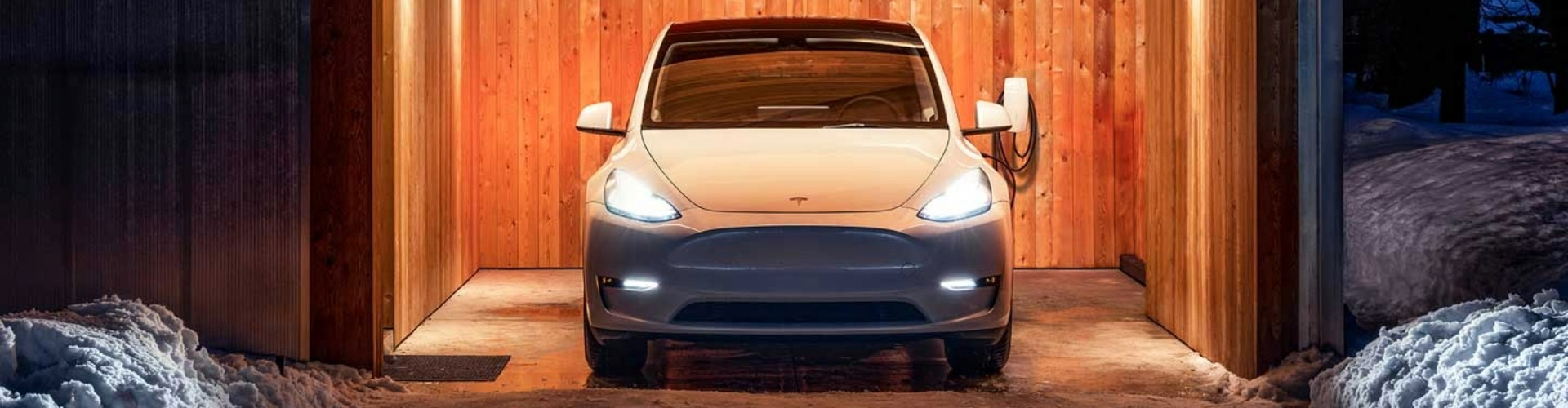 A white Tesla parked in a covered space with wooden paneling.