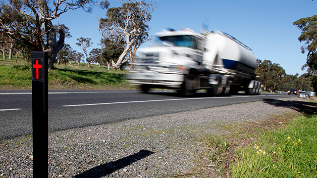 A truck speeds past a cross on a post