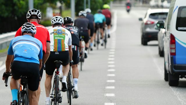 Group of cyclists riding down a road next to cars