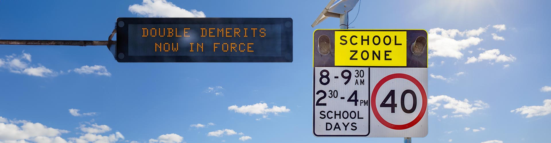 An LED sign reads "Double Demerits now in force" next to a School Zone sign on a background of fluffy clouds on a sunny day