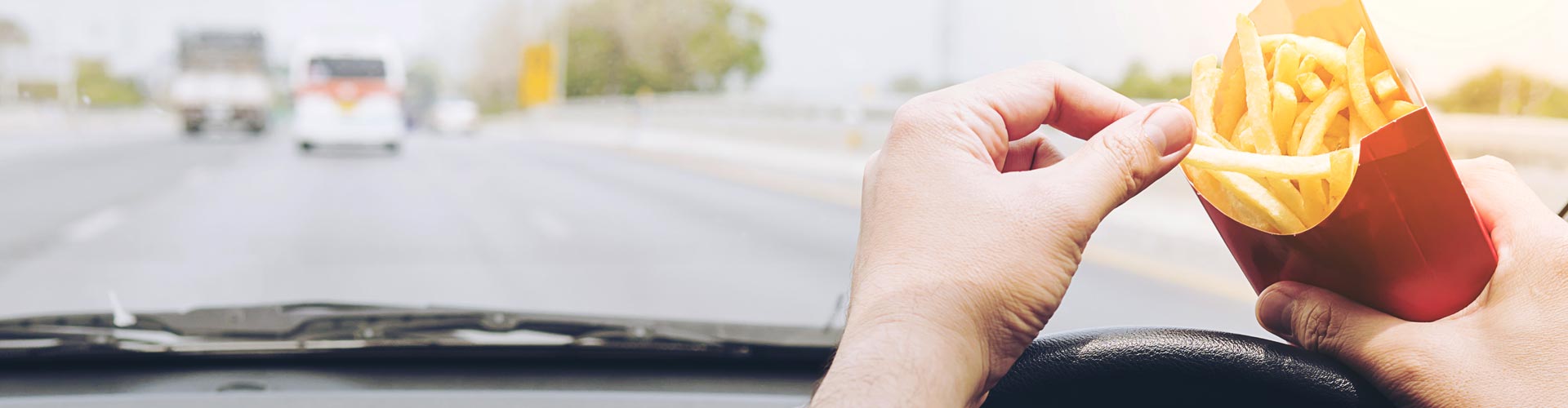 A hand reaches for chips while driving the steering wheel of a car