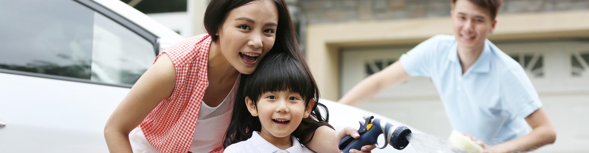 A mother helps her son wash the car as the father smiles in background