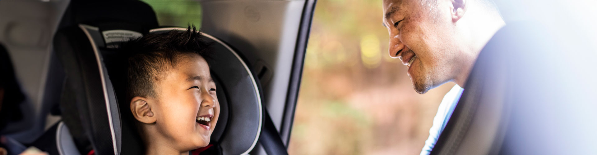 A father buckles his laughing child in to a car child seat in the back row