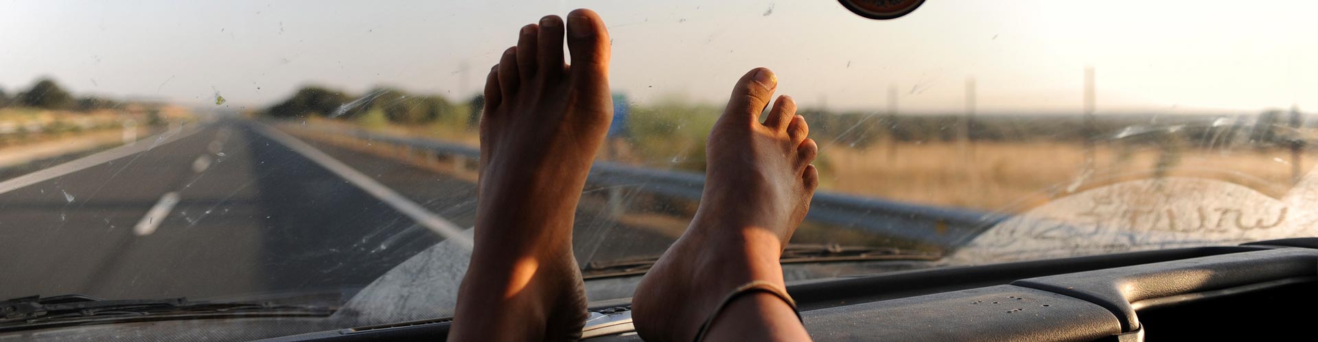 Bare feet on dash of car in front of dirty window