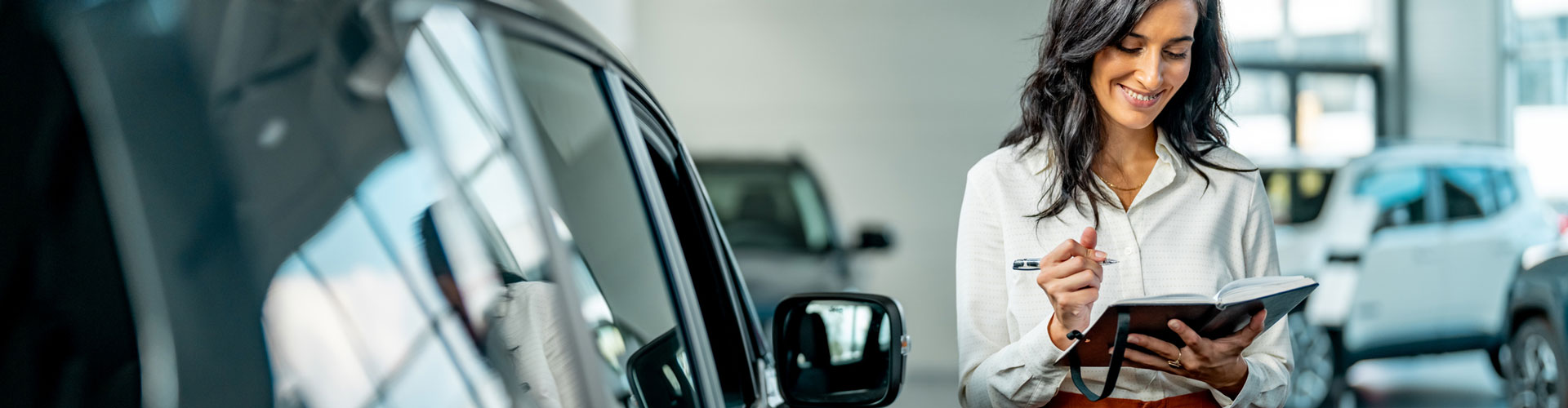 Car dealer with long hair wearing orange pants in showroom looking at a ledger book