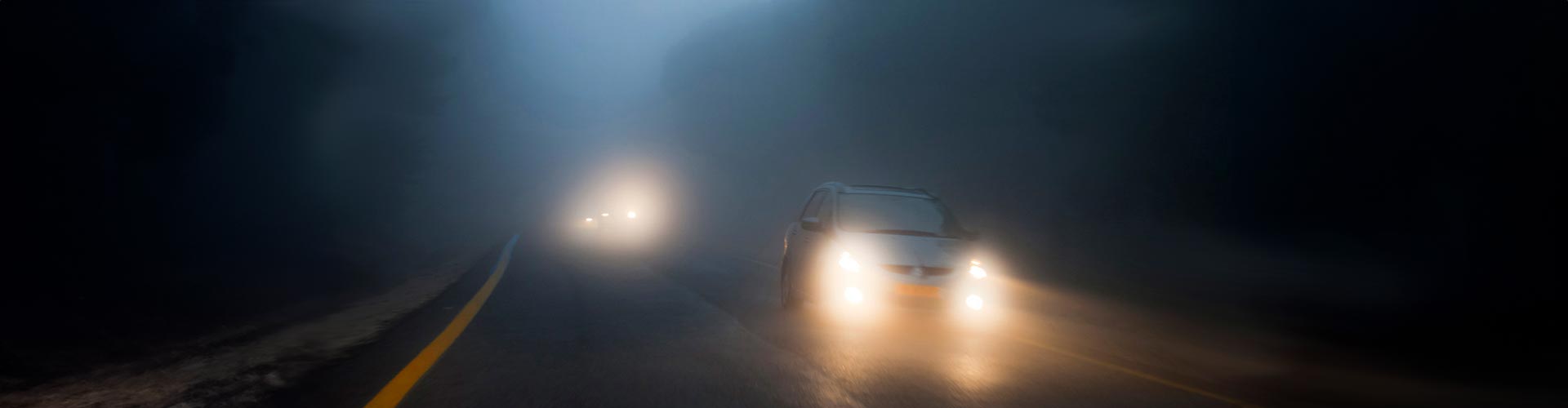 A car drives out of the dark with its fog lights on