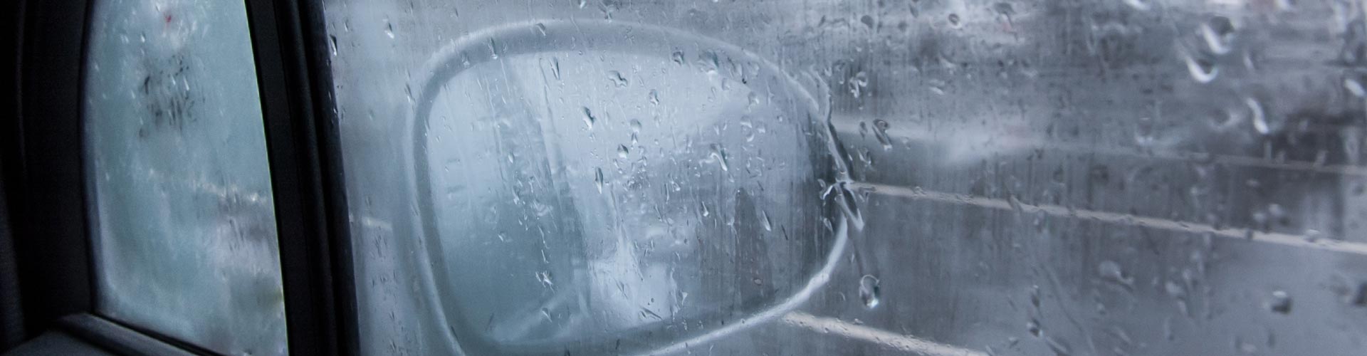 Foggy car window seen from inside of car with mirror on other side of glass