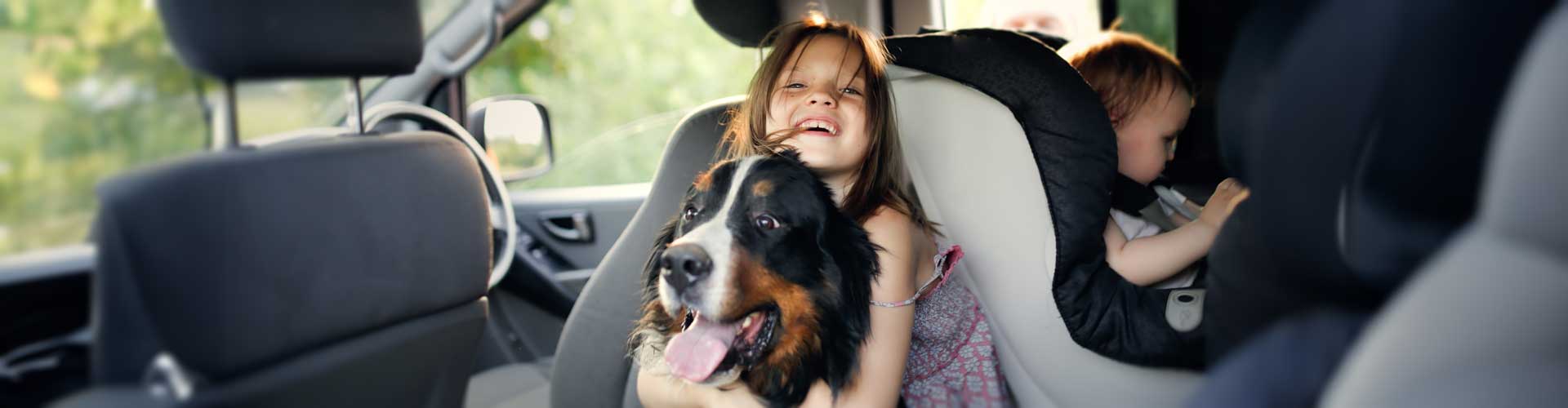 A young girl hugs her dog in the back of a car