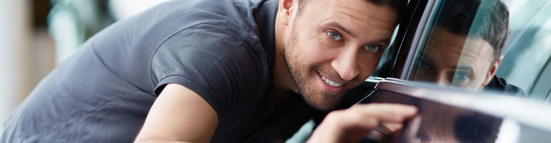 A young man smiles and looks intently at chrome detail on a car