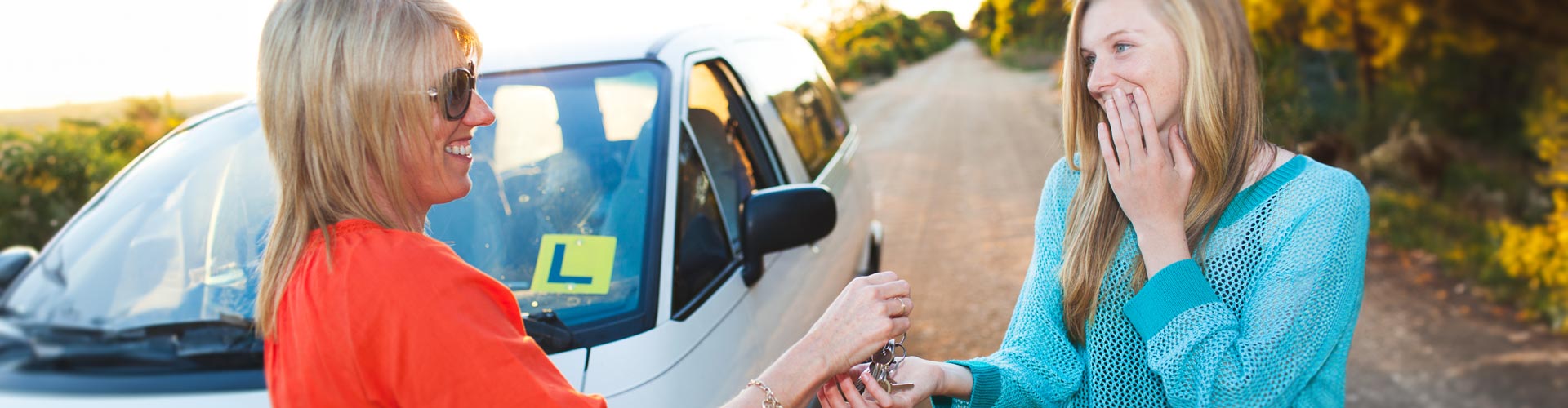 A mother gives her nervous daughter car keys. On the car is an L plate