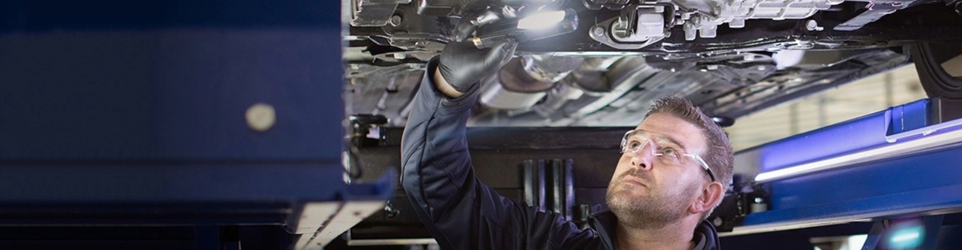 Motorserve mechanic motor mechanic stands under a car raised on a hoist and holds a light to inspect the underside