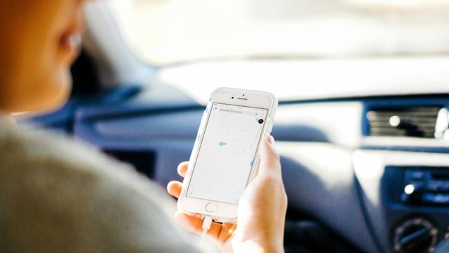 A hand of person in passenger seat holds mobile phone showing navigation