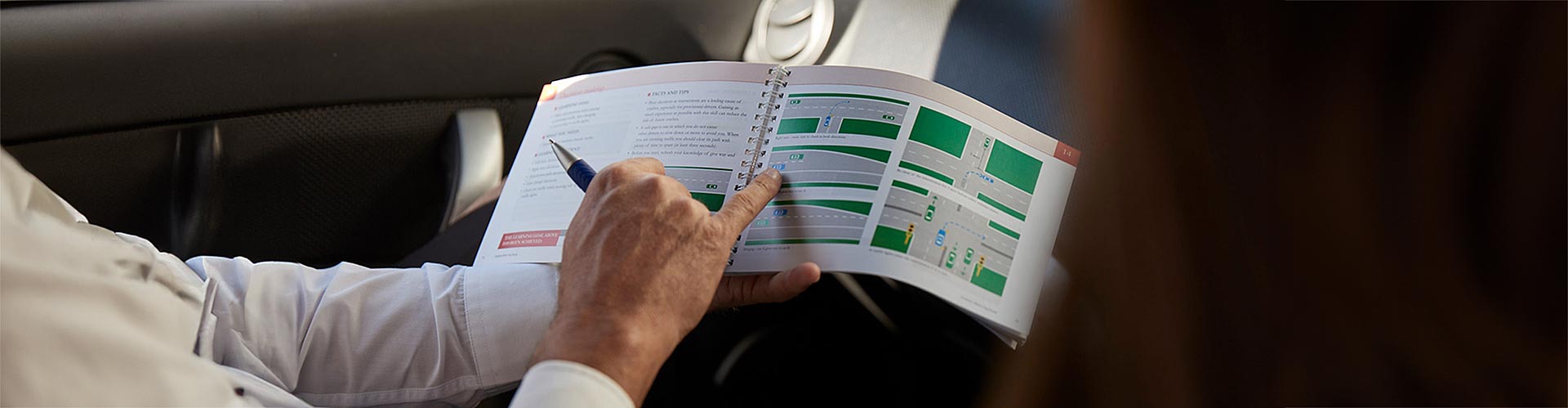 Instructor's hand points to a learner driver booklet