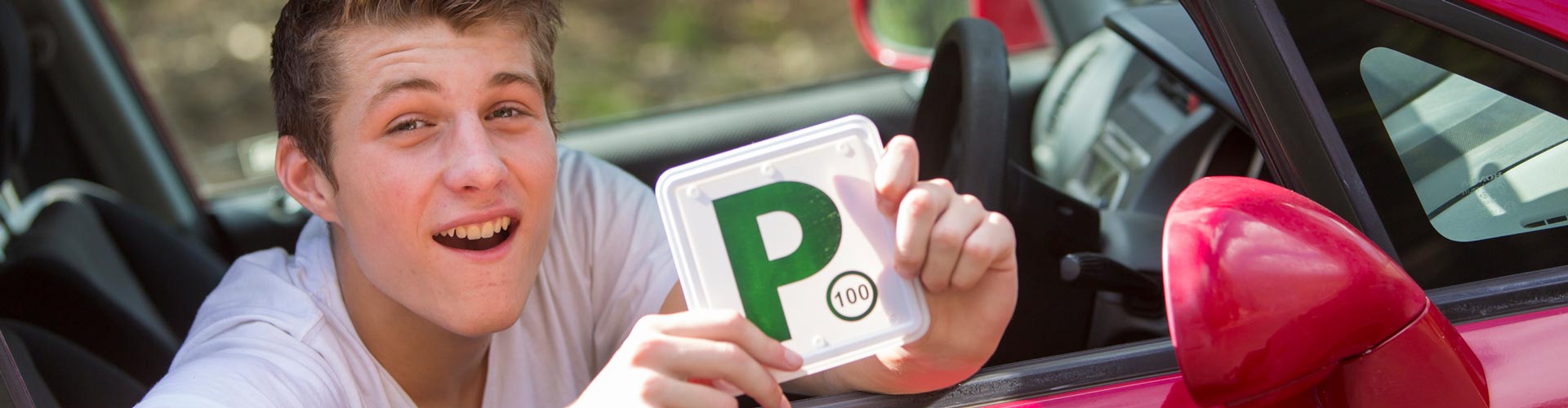 Young man with P plate sitting in red car