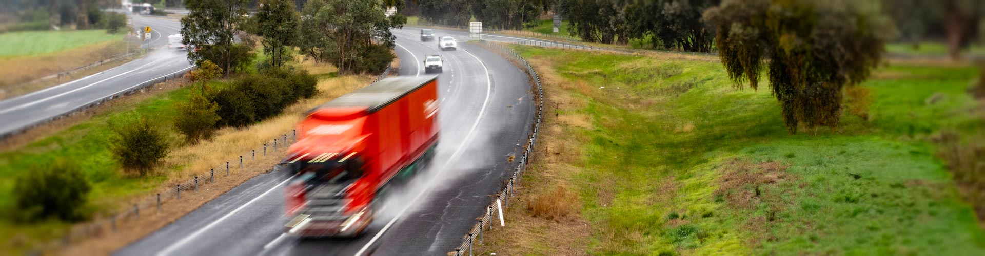 A red truck drives in the overtaking lane of a highway in front of other vehicles