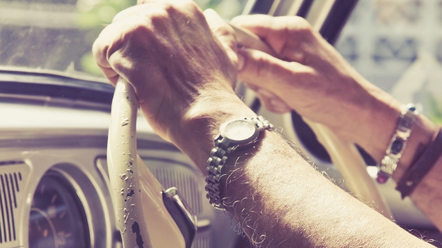 close up of a man's hands and arms and steering wheel of a classic vehicle