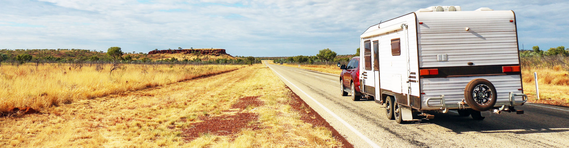 An SUV and caravan are parked on an outback road stretching into the distance