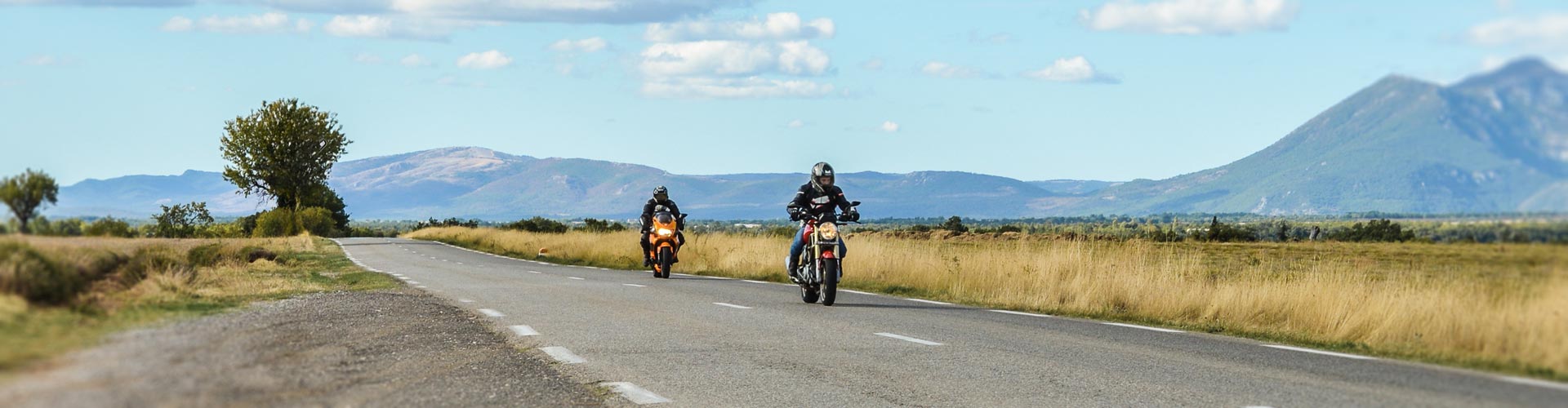 Two motorcyclist drive along a country road backed by mountains