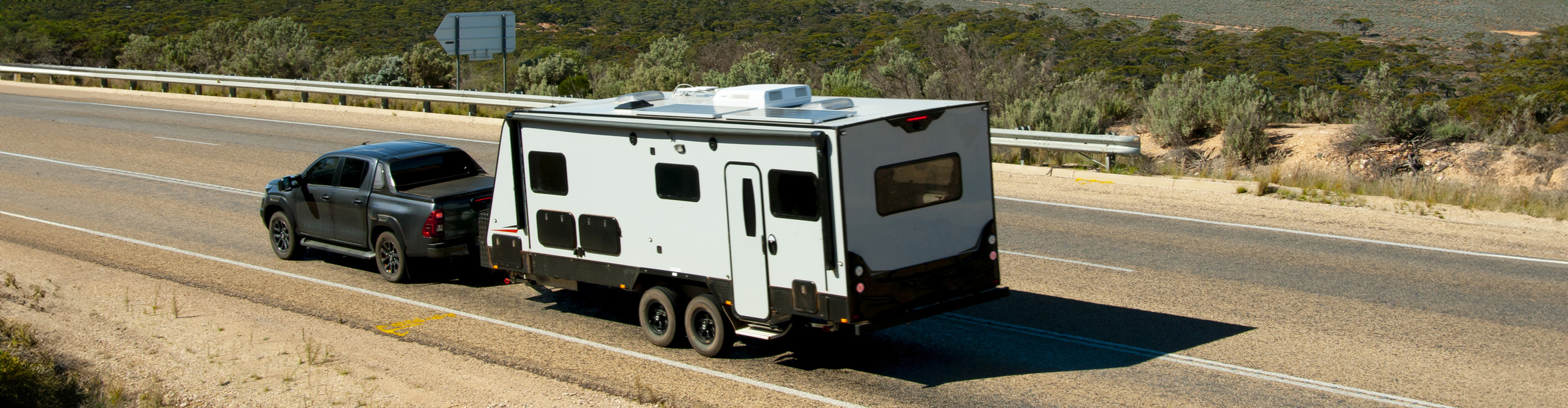 Black ute towing a white caravan with black accents along an outback road