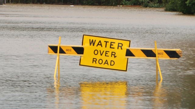 A sign that says "Water over road" sits in middle of flooded road