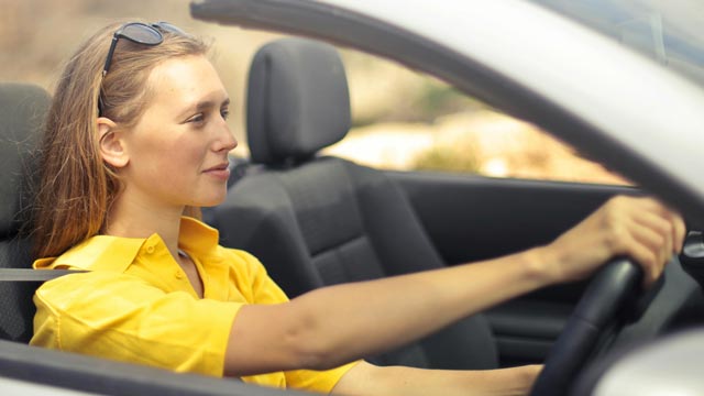Woman in yellow top sits in drivers seat of a convertible car