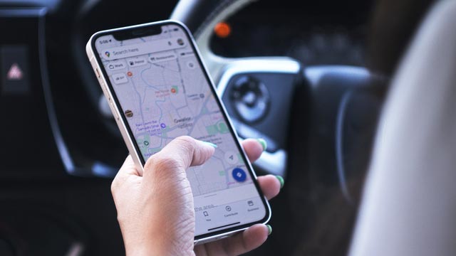 A woman's hand holds a phone while she is in the driver's seat
