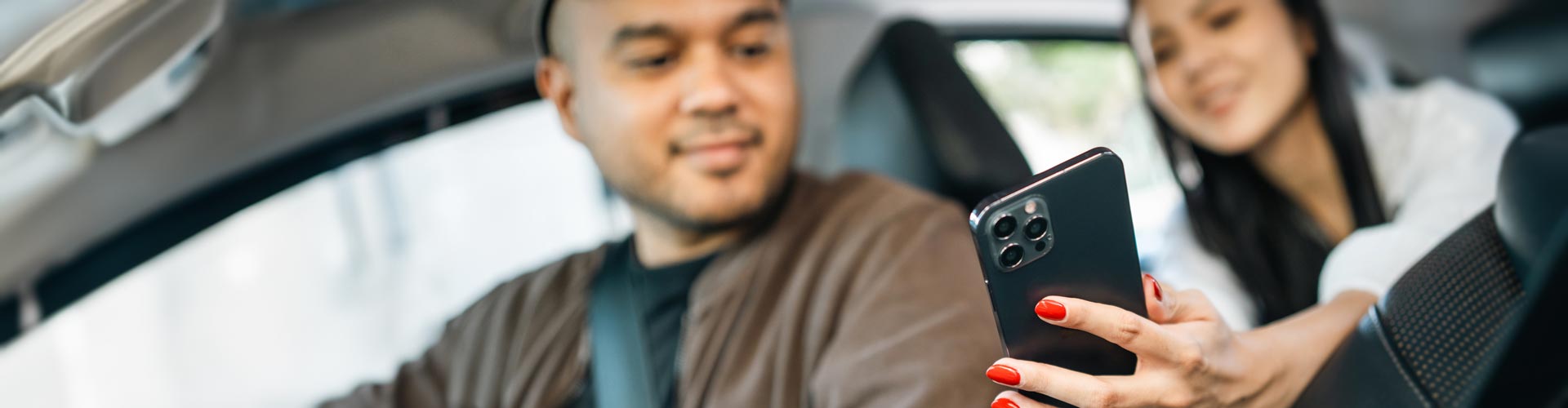 A woman in the back seat of car shows the driver something on her mobile phone