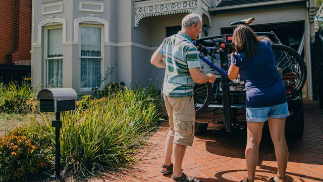 A man and woman securing a bike to a car bike rack