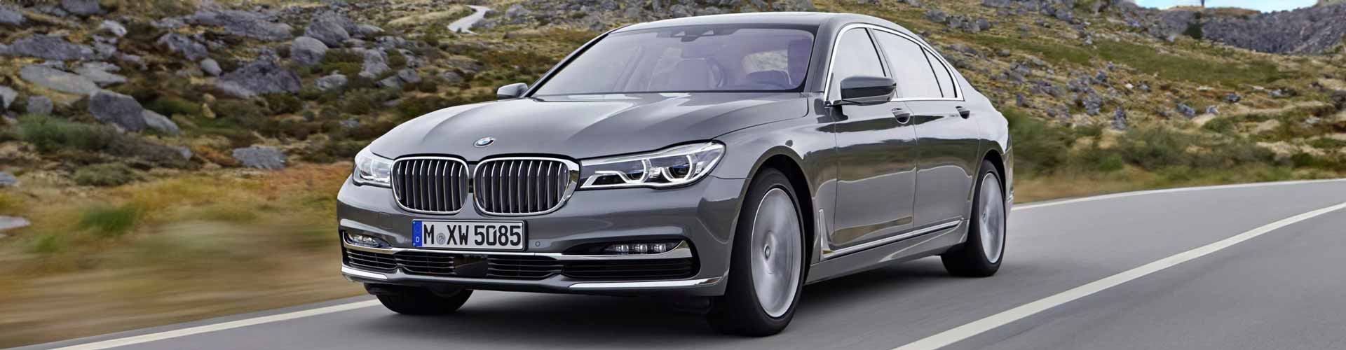 Front-angle view of a grey 7 series BMW sedan travelling along a road with a rocky mountain landscape in the background.