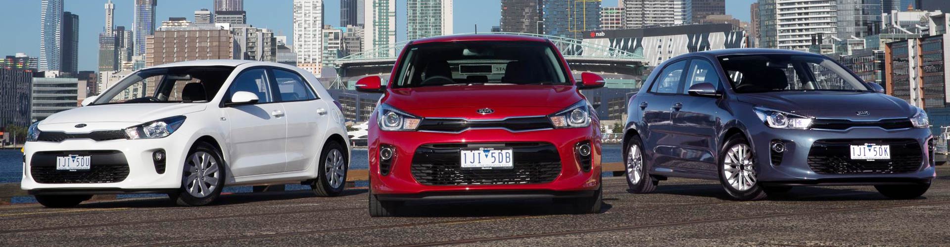 Three 2017 Kia Rio cars parked in front of a harbour scene