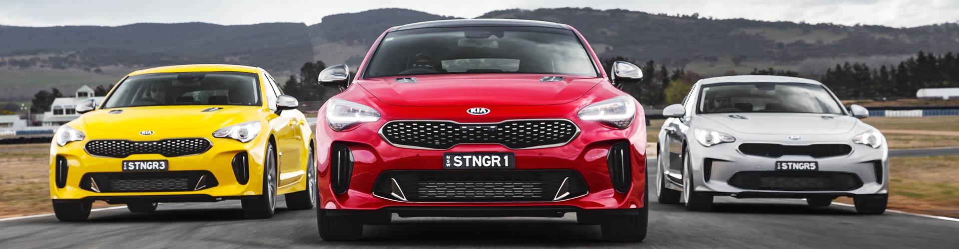 Yellow, red and grey 2018 Kia Stingers lined up on race track