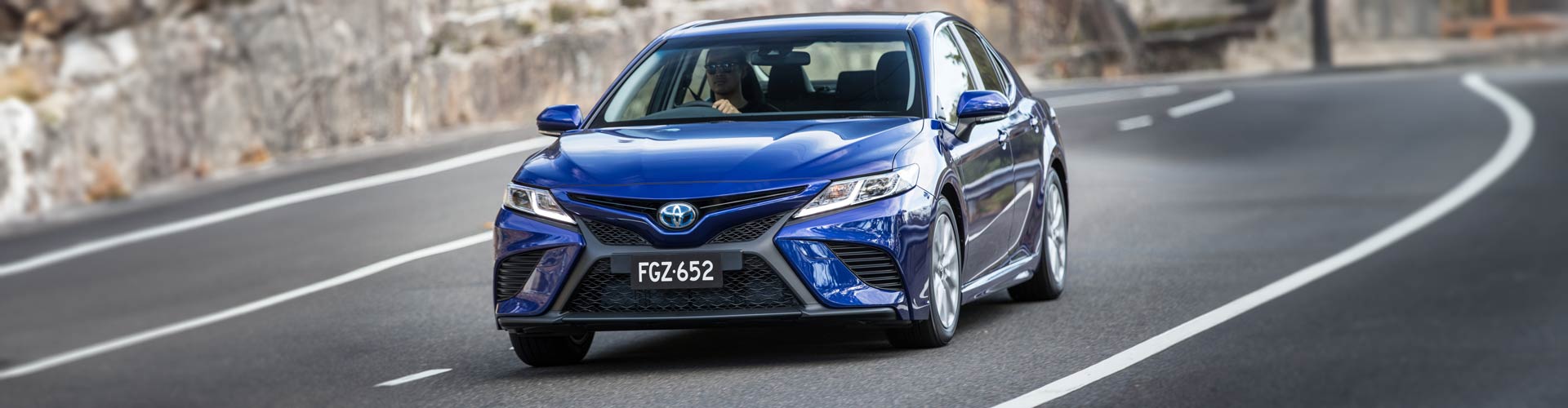 Blue 2018 Toyota Camry driving in front of sandstone wall