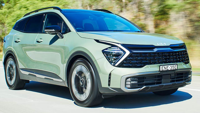 Green 2022 Kia Sportage driving on road past trees