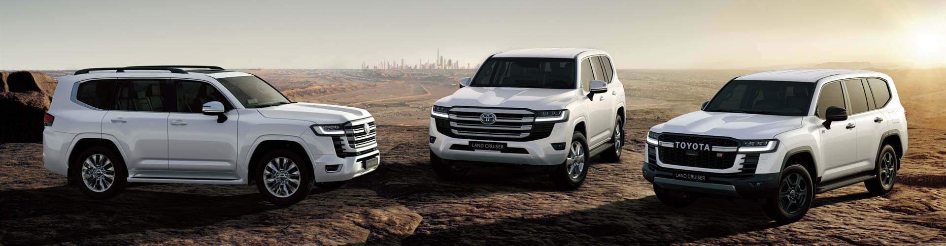 Three white 2022 Toyota LandCruisers parked on rocky outcrop at sunset