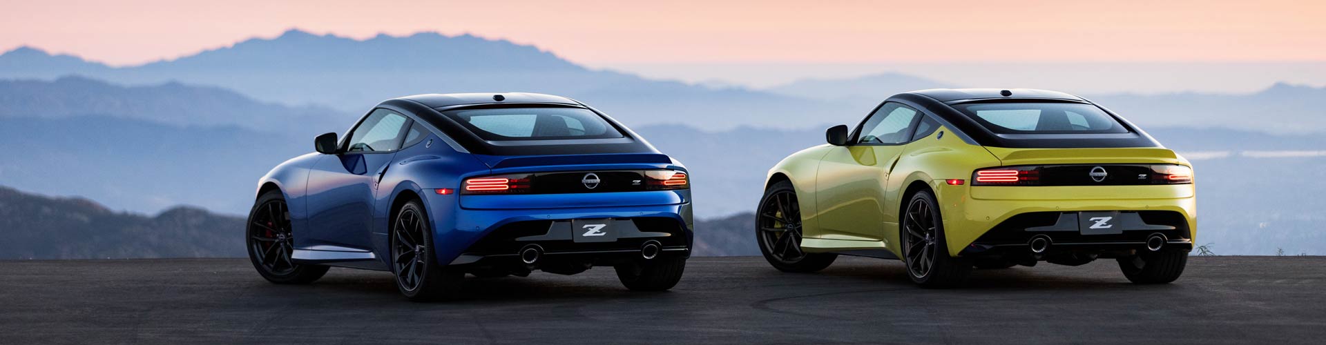 A blue and a yellow 2023 Nissan Z parked at sunset overlooking mountains