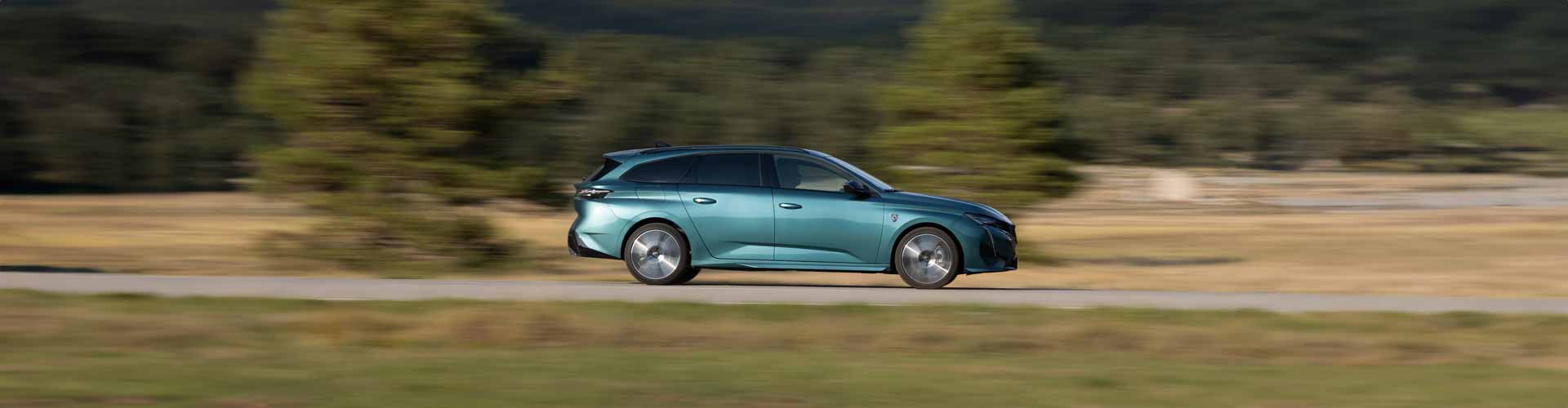 Teal 2023 Peugeot 308 GT Premium Wagon driving against blurred tree background