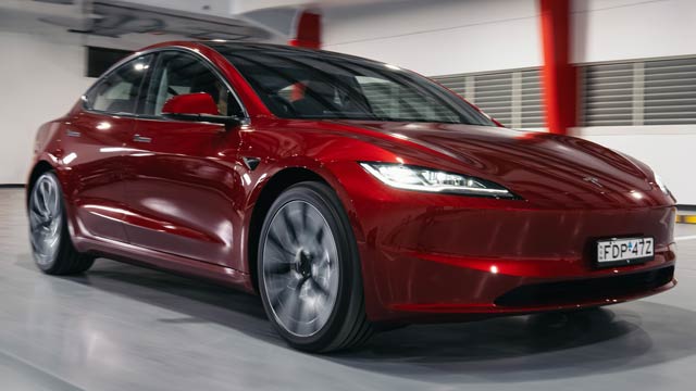 Red 2024 Tesla Model 3 driving inside a showroom