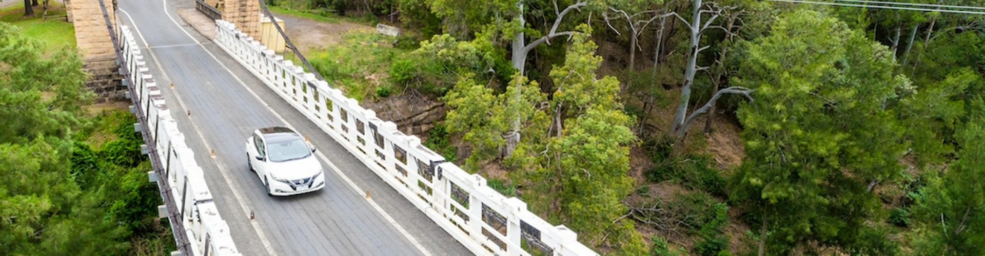 Ariel view of a car travelling across a bridge with white barrier fencing on either side.
