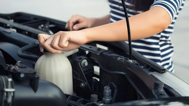 Close-up view of a woman checking a car's coolant level Close-up view of a woman checking a car's coolant level